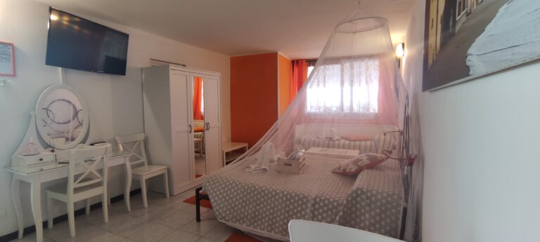 Immagine raffigurante la stanza Arancia, con candido baldacchino e dettagli arancioni.